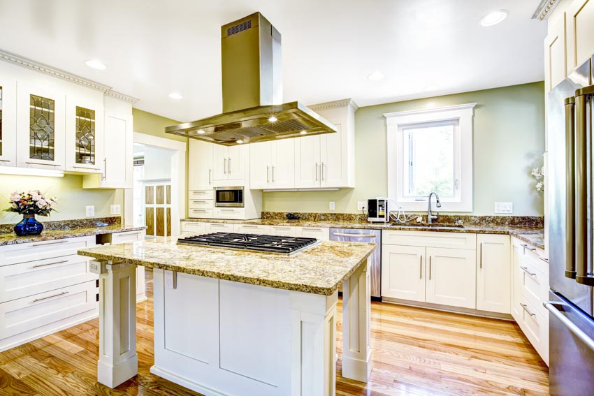 Kitchen with light sage walls, center island, range hood, stove, countertops, cabinets, and window