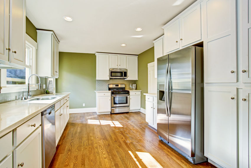 Kitchen with refrigerator, sage painted walls, wood flooring, white cabinetry, stove, oven, and countertops